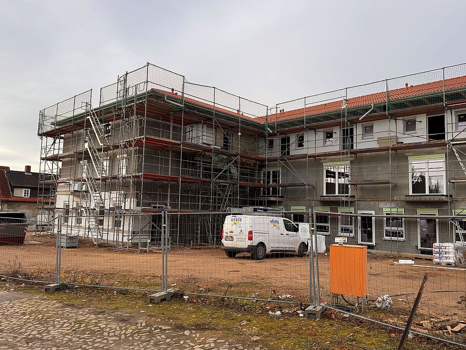Ein Quartiershaus wird von einem Baugerüst umgeben. Das Gebäude ist teilweise verdeckt, während Bauarbeiten stattfinden. Rundherum sind Materialien und Geräte einer Baustelle zu sehen.