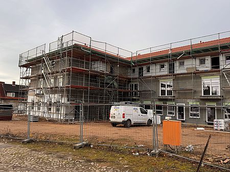 Ein Quartiershaus wird von einem Baugerüst umgeben. Das Gebäude ist teilweise verdeckt, während Bauarbeiten stattfinden. Rundherum sind Materialien und Geräte einer Baustelle zu sehen.