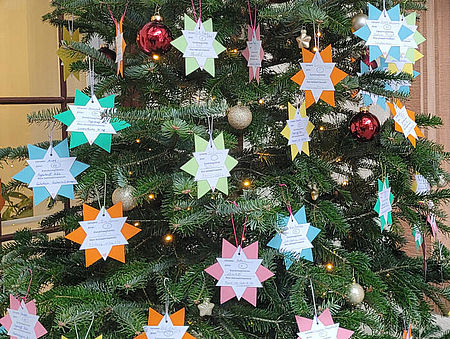 Weihnachtsbaum mit angehängten Papiersternen, auf denen die Kinderwünsche stehen