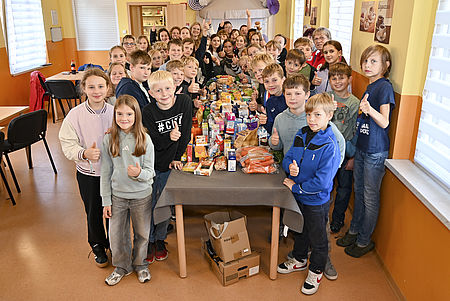Die fünften und sechsten Klassen des Bördegymnasiums in Wanzleben haben bei der Tafel im Sozialen Zentrum „Alter Bahnhof“ ihre traditionellen Erntedankspenden abgegeben. Eine Gruppe Kinder steht an einer langen Tafel voll mit gespendeten Lebensmitteln