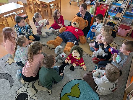 Mehrere Kindergartenkinder sitzen im Kreis um drei Stoffpuppen.