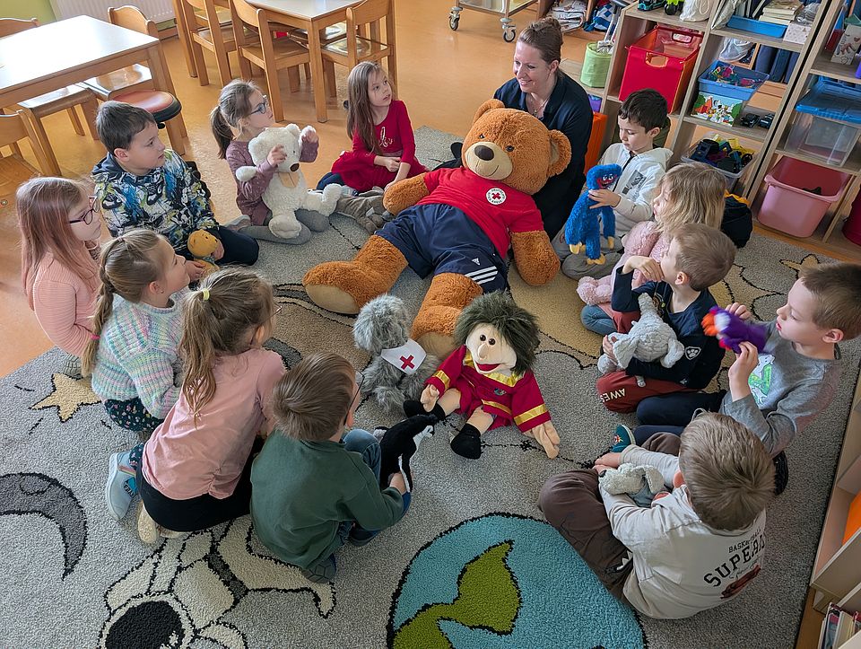 Mehrere Kindergartenkinder sitzen im Kreis um drei Stoffpuppen.
