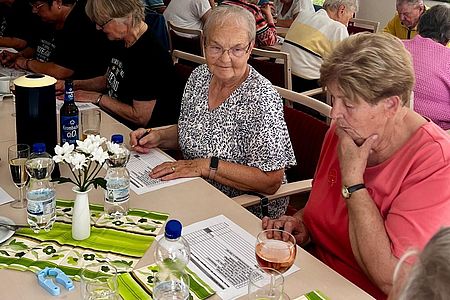 Zwei Seniorinnen sitzen über einem Fragebogen und überlegen.