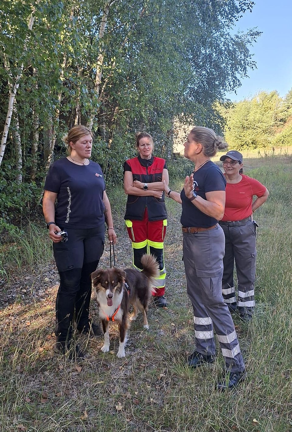Gespräch bei der Mantrail-Ausbildung: Patrizia Olbricht (links) redet mit der Ausbilderin Silke Ahlquist(rechts) aus Hamburg Vier Frauen und ein Hund stehen auf einem Waldweg. Die Frauen besprechen sich.