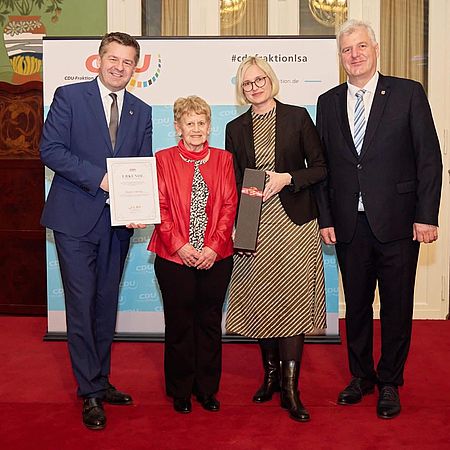 4 Personen stehen vor einer Tafel und halten Urkunden