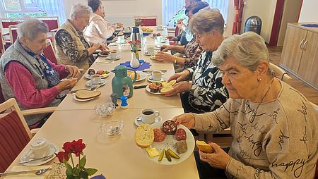 mehrere Seniorinnen sitzen an einer Tafel und haben Teller mit Wurst vor sich