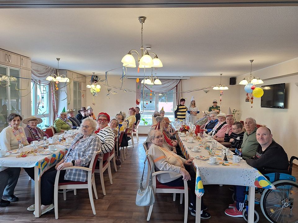 mehrere Seniorinnen und Senioren sitzen an zwei langen Tafeln, die nach Faschingsart geschmückt sind