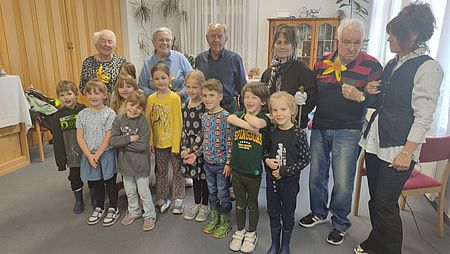 eine Gruppe Kita-Kinder stehen vor vier Senioren mit Blumensträußen