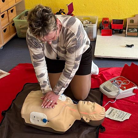 Eine Frau reanimiert ein Übungsmodell mit angeschlossenem Laiendefibrillator