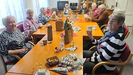 Senioren sitzen an weihnachtlicher Kaffeetafel und halten Teelichtkerzen hoch
