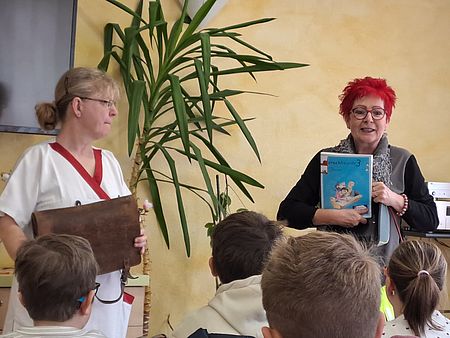 Schule gestern und heute - Ein Projekt mit Tradition im PflegeheimOsterweddingen 2 Frauen stehen vor einem Publikum und zeigen alte Schulhefte