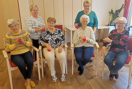 Vier sitzende und zwei stehende Seniorinnen mit roten Igelbällen