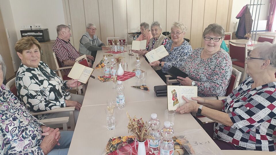 Kaffeenachmittag in der DRK-Begegnungsstätte Mehrere Senioren sitzen an einer Tafel und halten Poesiealben in den Händen