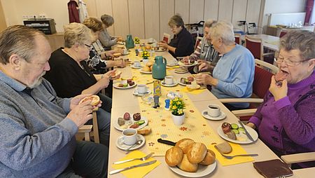 Mehrere Senioren sitzen an einer Tafel und essen Wurstbrötchen
