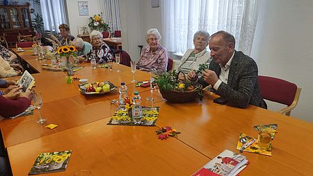 Ältere Menschen sitzen zusammen an der Kaffeetafel und sehen sich Bilder und Erntekörbchen an