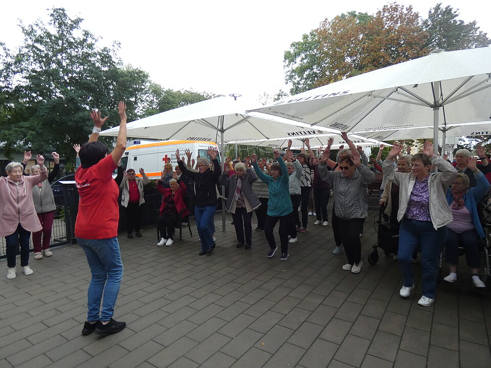 Zehn Gymnastikgruppen nahmen am Sportfest teil. Zahlreiche Senioren machen Sportübungen im freien, wärend eine Leiterin im roten Shirt vorturnt.