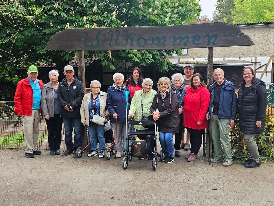 Die Tagespflege Osterweddingen zu Besuch im Staßfurter Zoo Eine Gruppe Senioren und BEtreuer stehen unter einem hölzernen Wilkommenschild