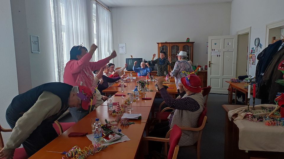 Faschingsparty in Langenweddingen mit kräftigem "Helau" mehrer Senioren sitzen und stehen an einer langen Tafel und strecken die Arme in dei Höhe