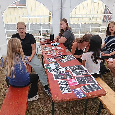 Kinder sitzen am Tisch und bemalen sich mit Tattoos