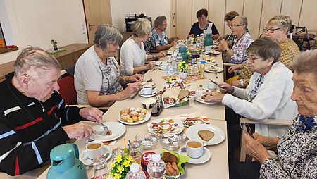 Mehrere Senioren sitzen an einer reich gedckten Kaffeetafel
