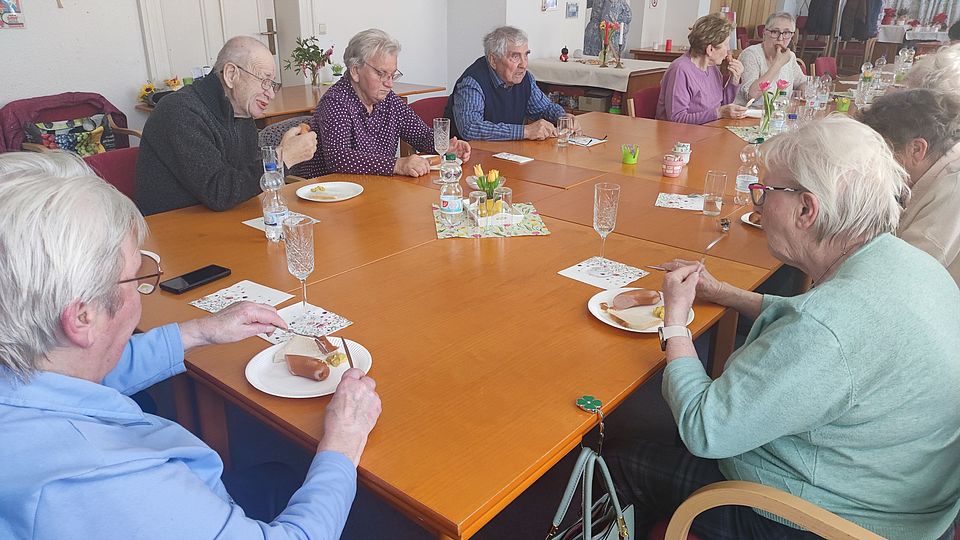 Senioren sitzen an einer Kaffeetafel und essen Würstchen