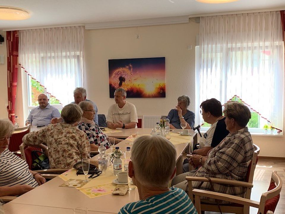 mehrere Personen sitzen an einer Tafel und hören einem Redner zu