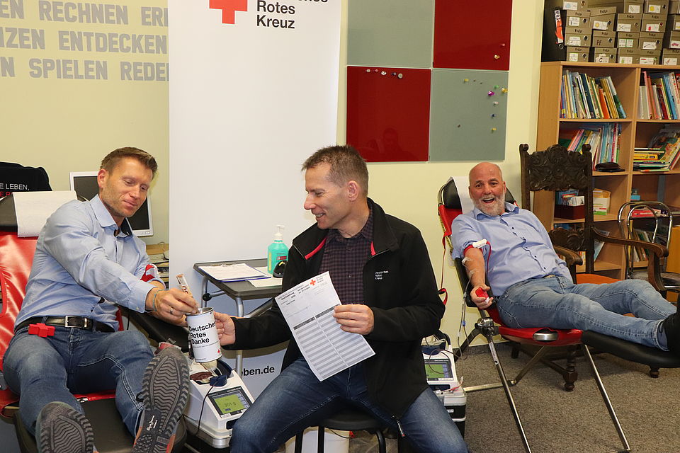 Zum Auftakt der Spendensammlung kam der Schirmherr Martin Tunsch (links) mit dem Vorstandsvorsitzenden Torsten Winkelmann (rechts) und dem Geschäftsführer Guido Fellgiebel zur Blutspende nach Ummendorf zwei Männer sitzen auf Blutspendestühlen. Einer gibt eine Spende in eine Spendendose