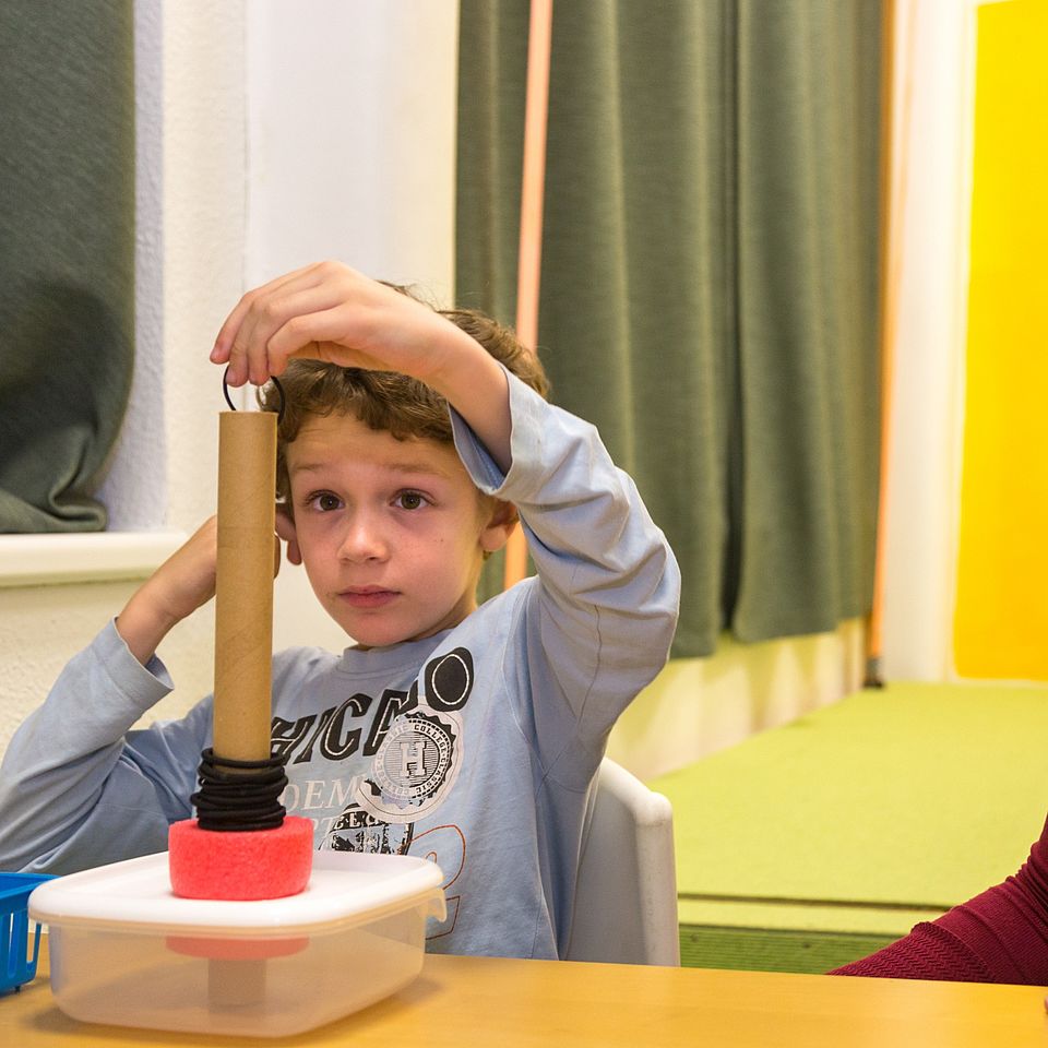 Ergotherapeut kleiner Junge stapelt Therapiematerieal übereinander