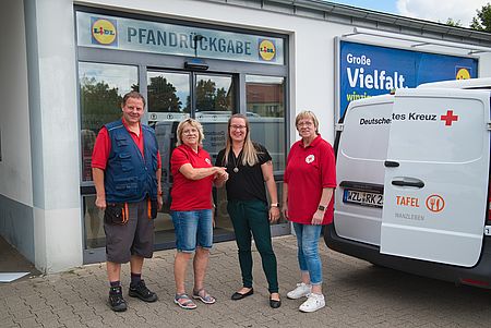 Drei Frauen und ein Mann stehen vor der Lidl-Pfandstation und reichen sich die Hände