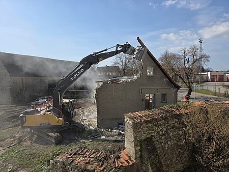 Ein Bagger greift in den halb abgerissenen Giebel eines Wohnhauses