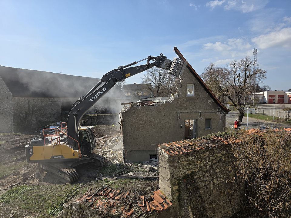 Ein Bagger greift in den halb abgerissenen Giebel eines Wohnhauses